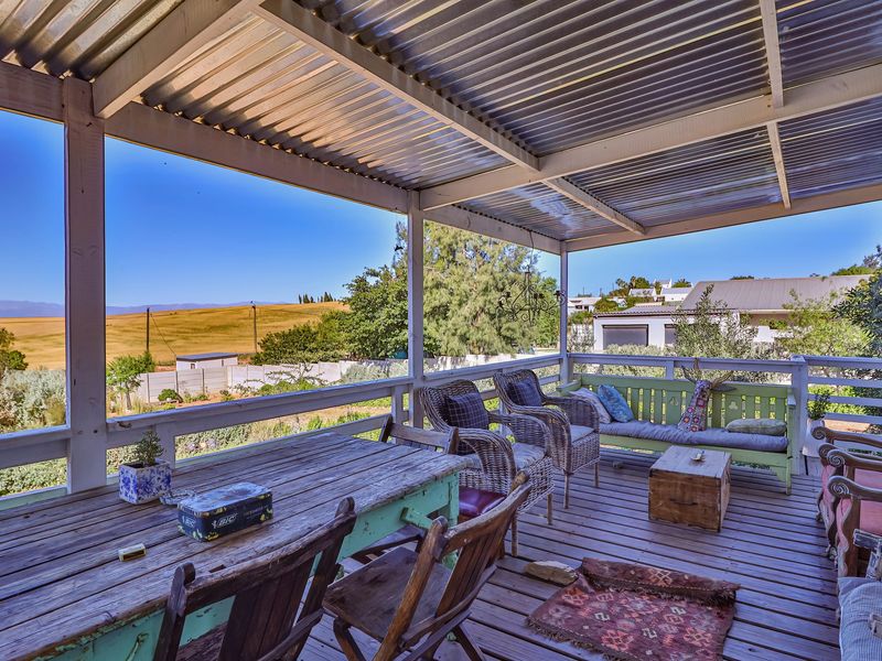 Covered outdoor patio featuring timber decking and a corrugated metal roof, offering expansive views of the surrounding landscape.