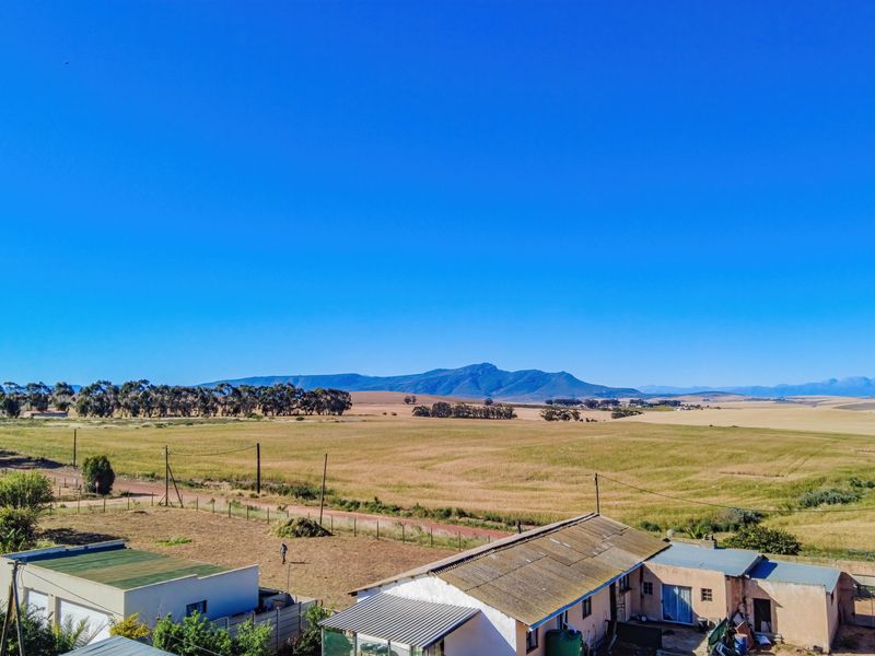 Elevated aerial view showcasing expansive rural landscape, mountain vistas, and the property's exterior roof and yard area.
