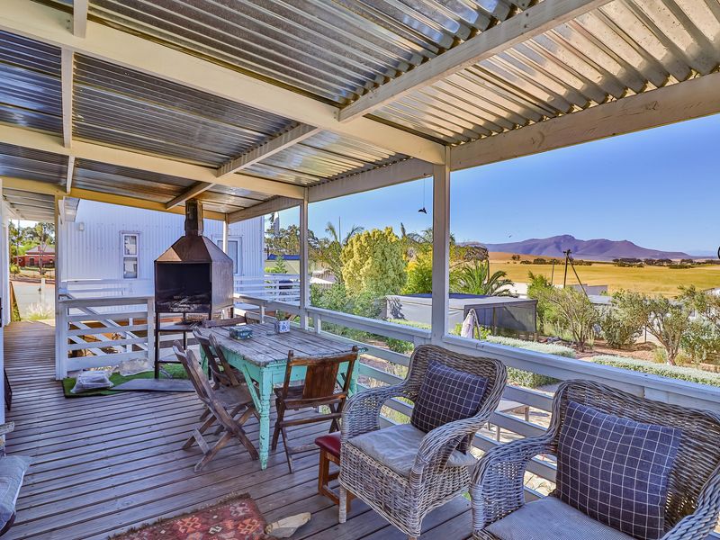 Covered outdoor patio featuring timber decking, a built-in braai, and scenic rural views, providing an ideal space for outdoor entertaining.
