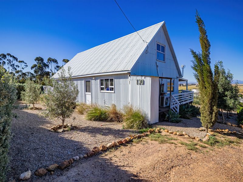 A charming cottage featuring corrugated metal cladding, a pitched roof, and a timber deck, set within a low-maintenance gravel garden.