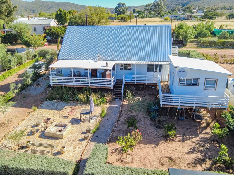 Aerial view of a property featuring a corrugated metal roof, raised timber decking, and a stone-paved outdoor entertainment area with a built-in fire pit.