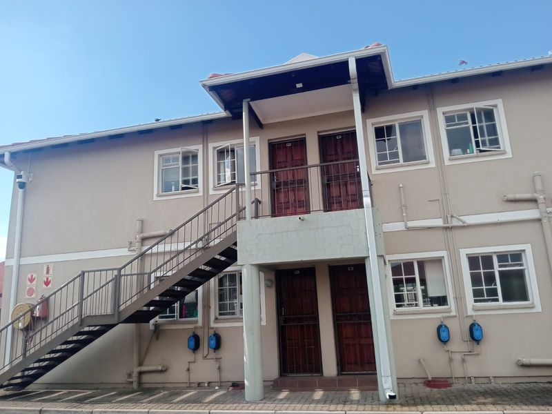 Exterior view of a two-story flat complex featuring a metal staircase, security gates, and external plumbing fixtures.