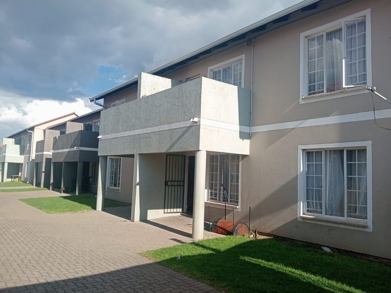 Exterior view of a multi-story flat complex featuring balconies, paved walkways, and established lawn areas.