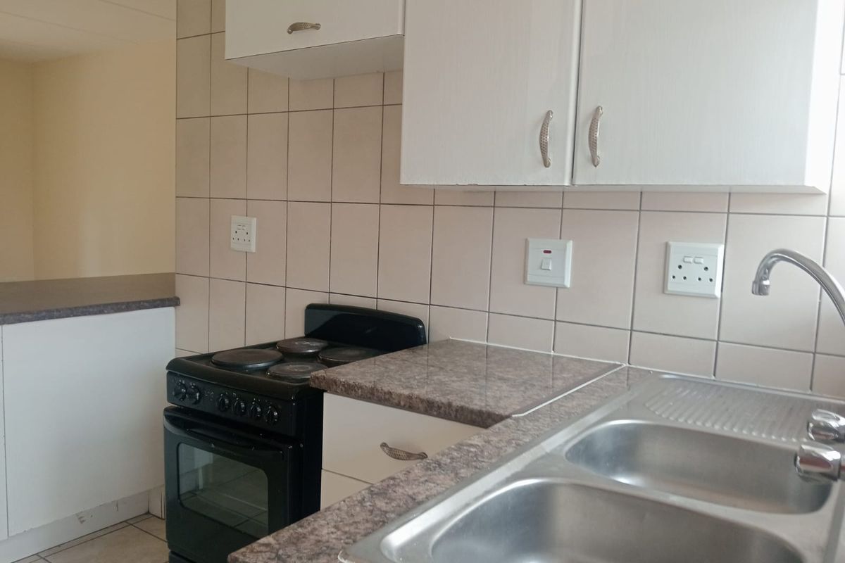 A functional kitchen featuring laminate countertops, a double bowl stainless steel sink, and a freestanding electric stove with tiled splashbacks.