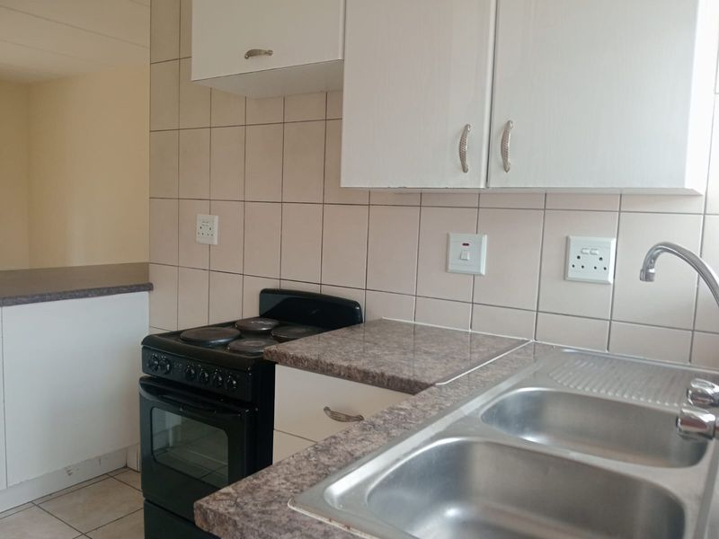 A functional kitchen featuring laminate countertops, a double bowl stainless steel sink, and a freestanding electric stove with tiled splashbacks.