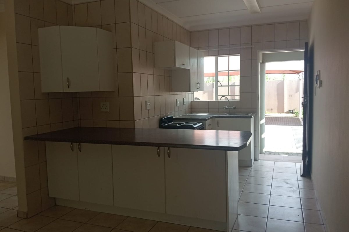 A functional kitchen featuring built-in cabinetry, tiled splashbacks, and a breakfast counter, with direct access to an outdoor area.