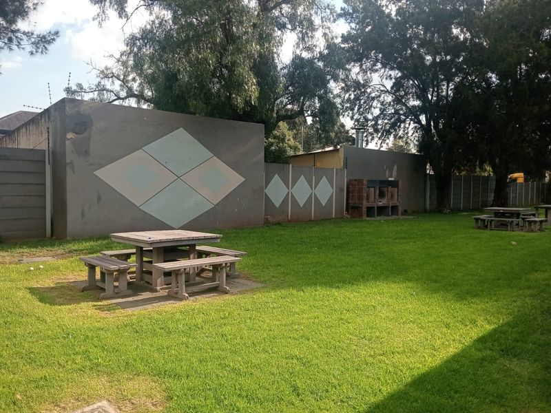A communal garden area featuring a lawn, perimeter wall with electric fencing, and a built-in brick braai facility.