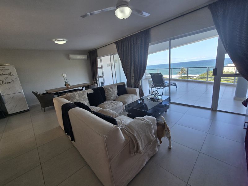 Spacious open-plan living area featuring tiled floors, ceiling fan, and large sliding glass doors opening onto a balcony with ocean views.