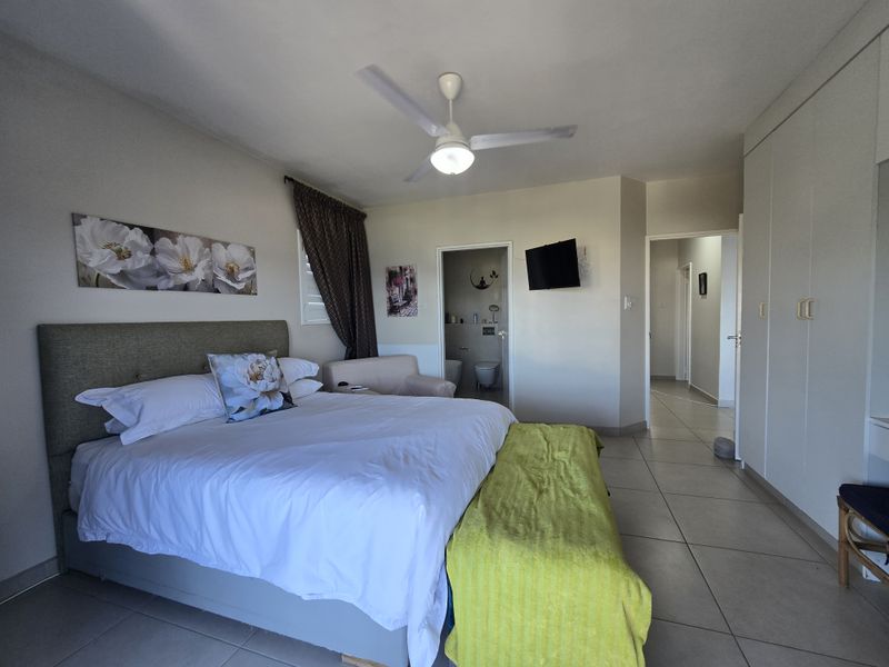 Spacious bedroom featuring tiled flooring, built-in cupboards, a ceiling fan, and direct access to an en-suite bathroom.