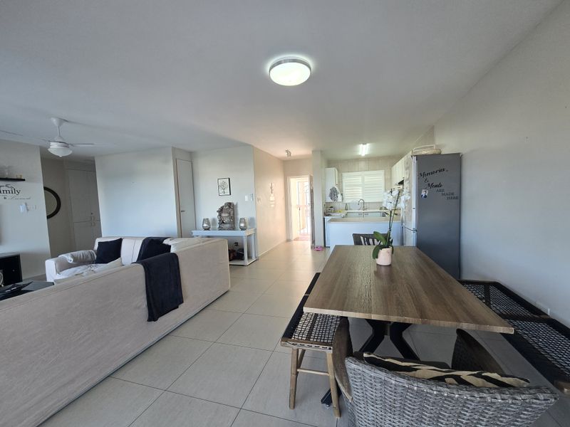 Spacious open-plan living and dining area featuring neutral tiled flooring, a ceiling fan, and a functional kitchen with built-in cabinetry.