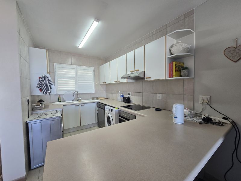 Functional kitchen featuring built-in cabinetry, laminate countertops, tiled splashbacks, and integrated appliances including a hob, oven, and extractor fan.