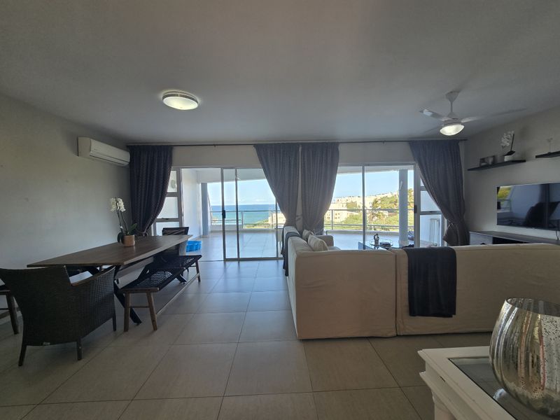 Spacious open-plan living and dining area featuring large sliding glass doors that open onto a balcony with ocean views.
