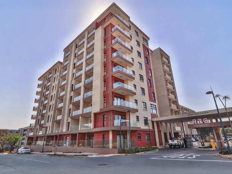 A modern multi-story apartment complex featuring glass balconies, a secure entrance gatehouse, and well-maintained exterior brick and concrete finishes.
