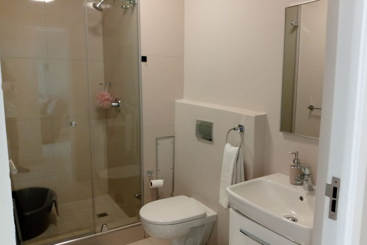 A modern bathroom featuring a glass-enclosed shower, wall-mounted toilet, and a vanity basin with a mirror.