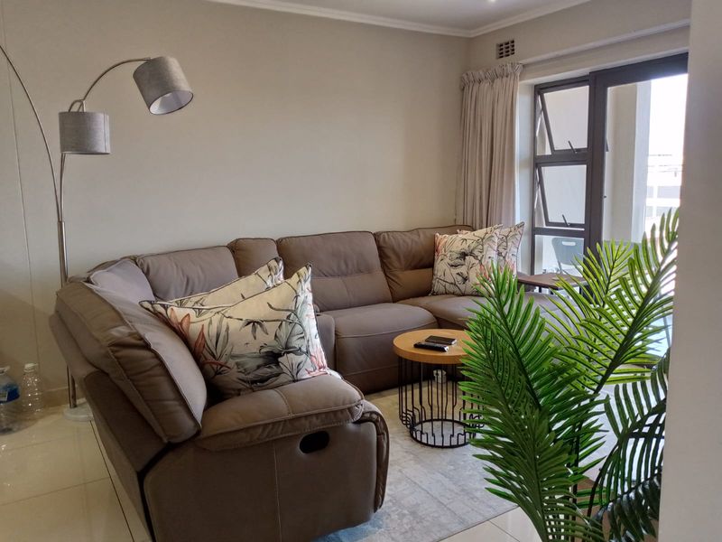 A comfortable living room featuring tiled flooring, recessed lighting, and large aluminium windows that provide natural light.