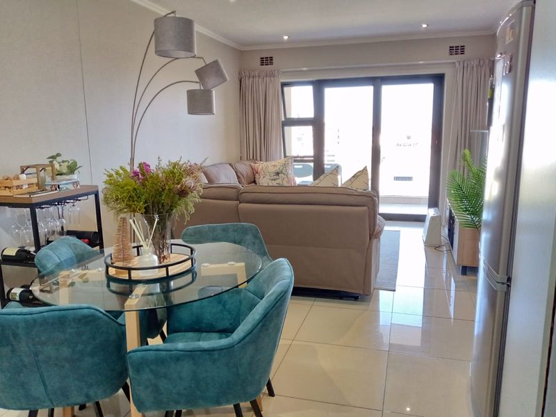 Bright open-plan living and dining area featuring large format floor tiles and a sliding glass door leading to an outdoor balcony.