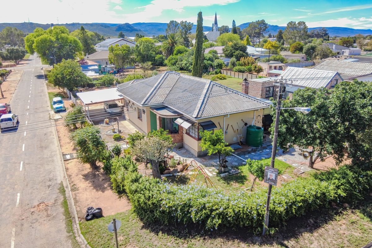 Aerial view of a residential property featuring a tiled roof, carport, and established garden with perimeter hedging in a suburban setting.