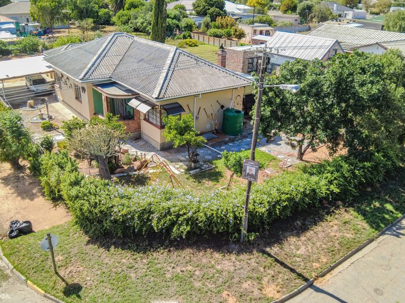 Aerial view of a residential property featuring a tiled roof, a carport, a rainwater tank, and a landscaped garden with perimeter hedging.