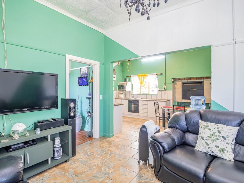 Open plan living area featuring tiled floors and a connected kitchen with built-in cabinetry, oven, and a fireplace, requiring cosmetic updates.