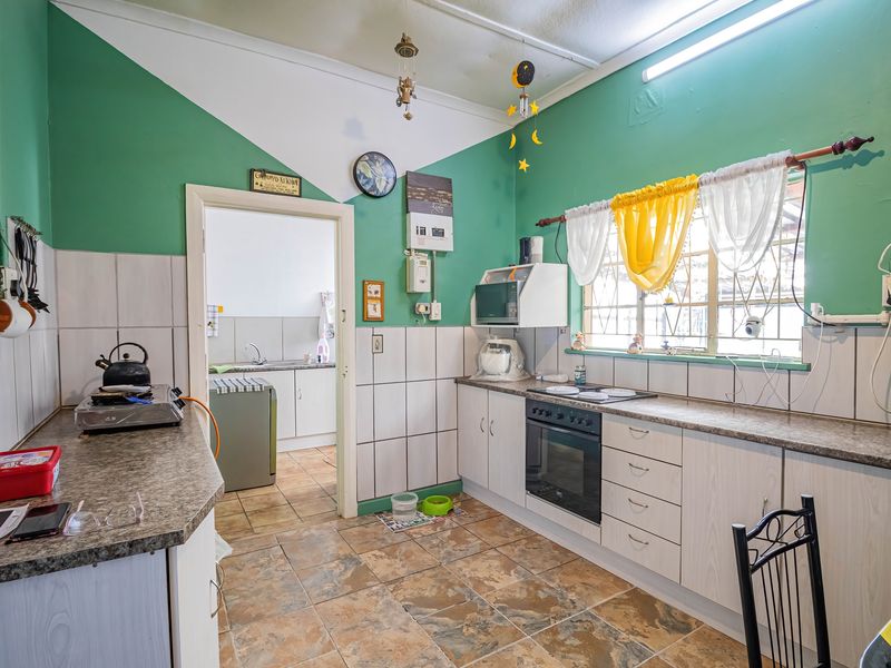 A functional kitchen featuring built-in cabinetry, an integrated oven and hob, tiled splashbacks, and a connected scullery area.