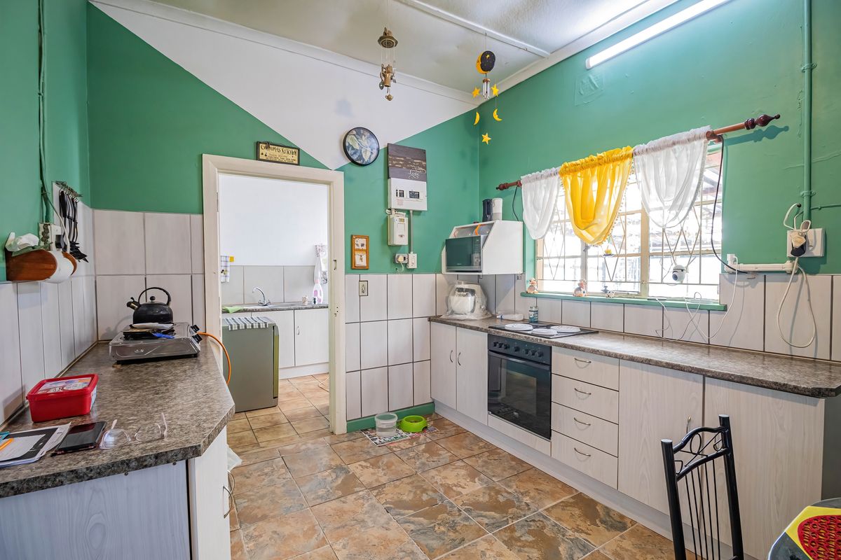 A functional kitchen featuring built-in cabinetry, an integrated oven and hob, tiled splashbacks, and a connected scullery area.