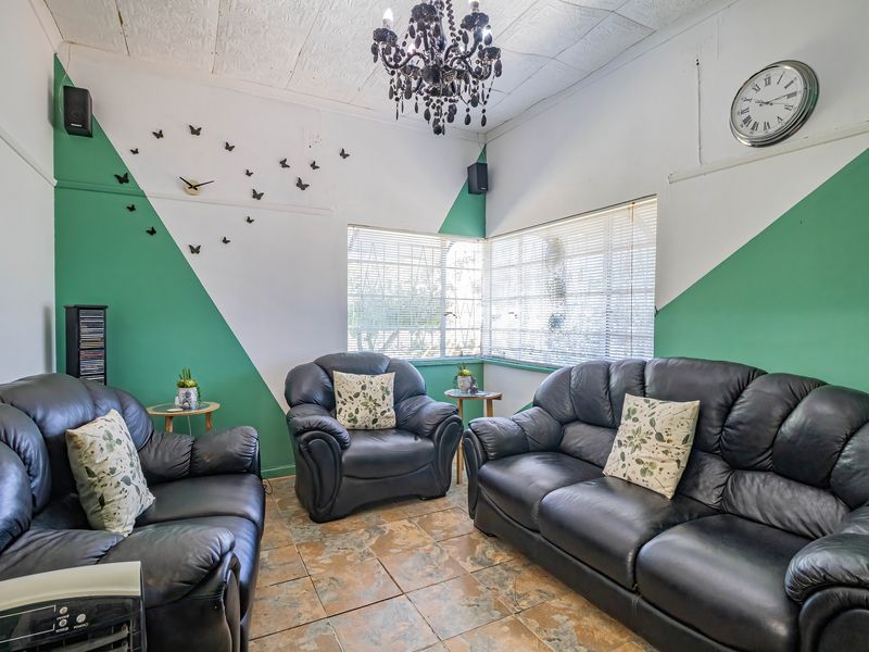 A living room featuring tiled flooring, venetian blinds, and a decorative ceiling with a chandelier, currently styled with a three-piece leather sofa set.