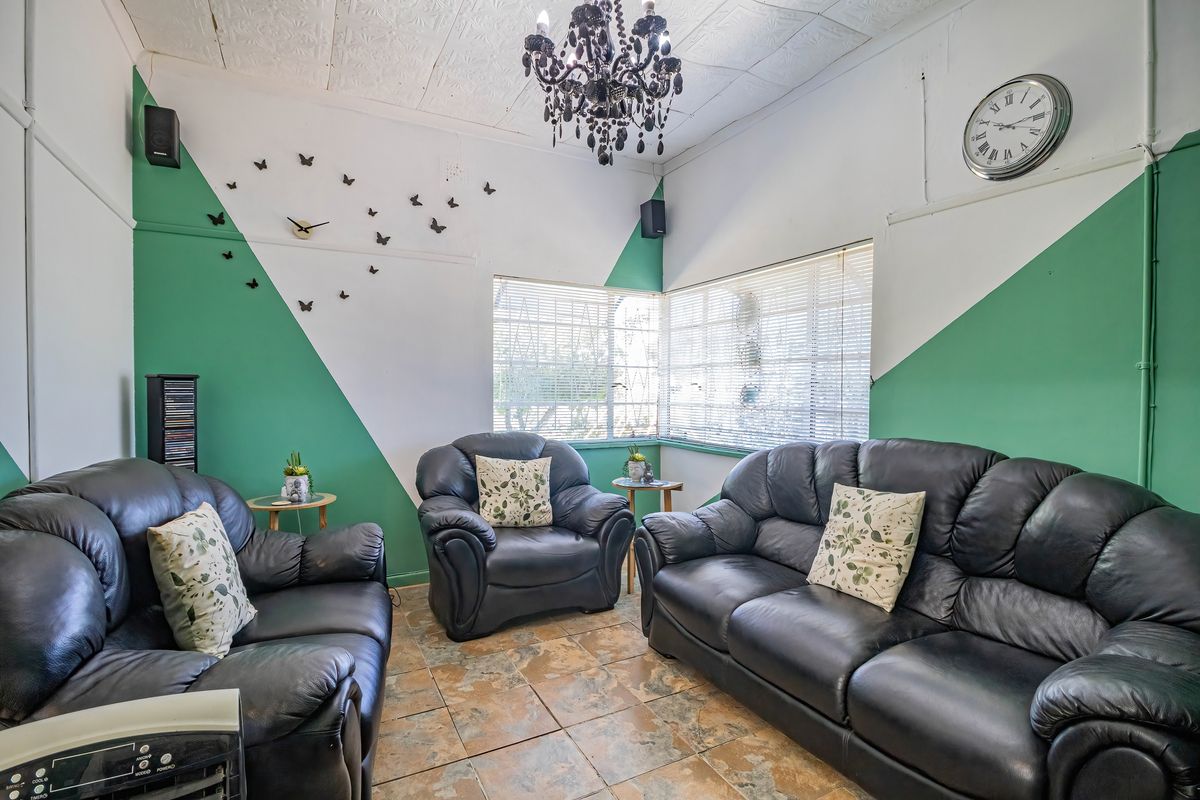 A living room featuring tiled flooring, venetian blinds, and a decorative ceiling with a chandelier, currently styled with a three-piece leather sofa set.