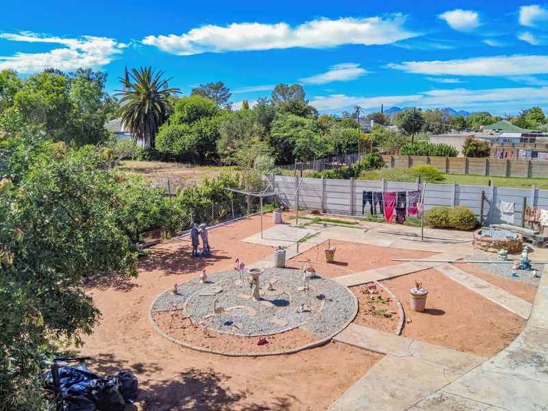 Spacious rear garden featuring a precast concrete boundary wall, paved pathways, and a central gravel feature, offering potential for landscaping.