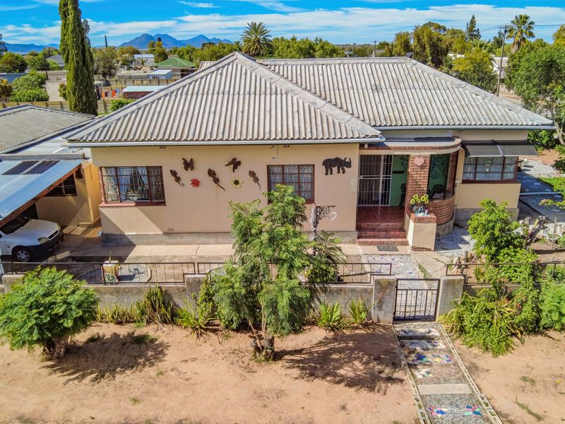 Aerial view of a single-story residential house featuring a corrugated metal roof, brick facade, and a front garden with a paved walkway.