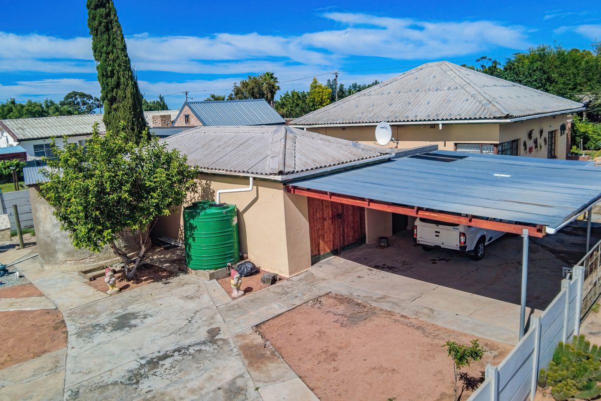 Rear exterior view showing a carport, concrete driveway, and water storage tank against a weathered building structure.