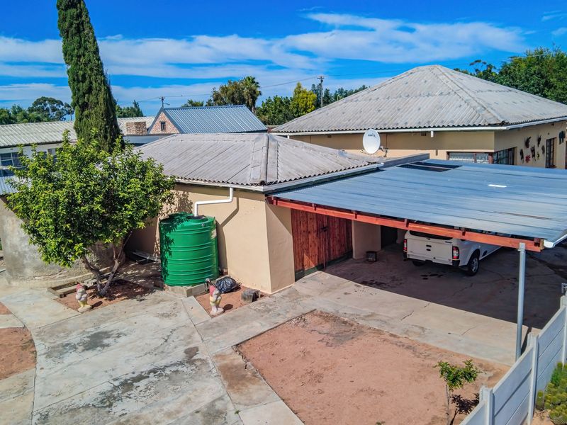 Rear exterior view showing a carport, concrete driveway, and water storage tank against a weathered building structure.