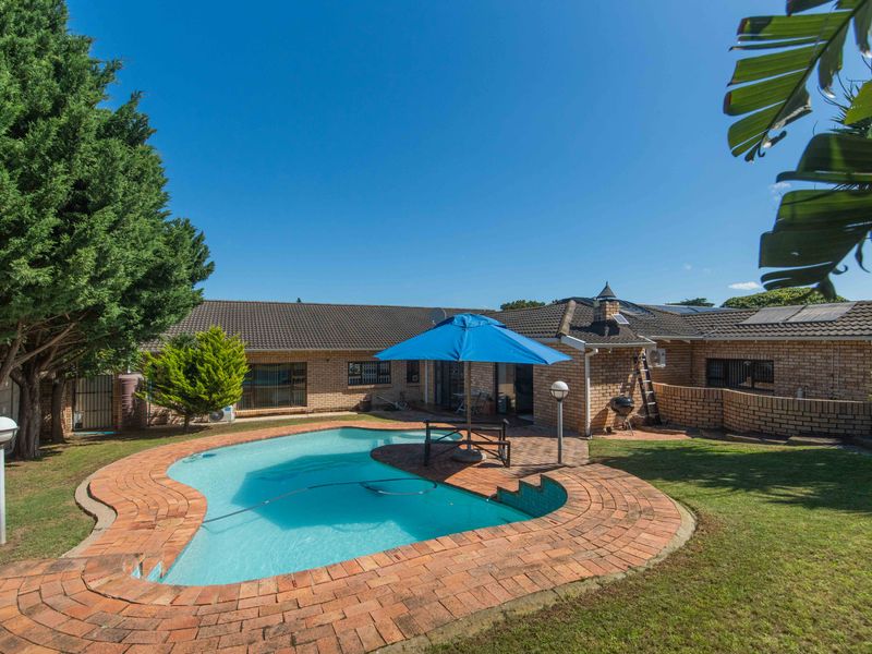 A spacious backyard featuring a swimming pool with brick paving, surrounded by a well-maintained garden and a brick-built house exterior.