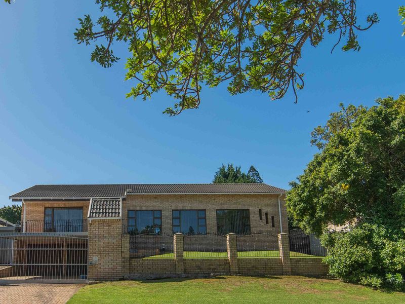 Front elevation of a brick house featuring a tiled roof, balcony, secure gated driveway, and a landscaped front garden with boundary walling.