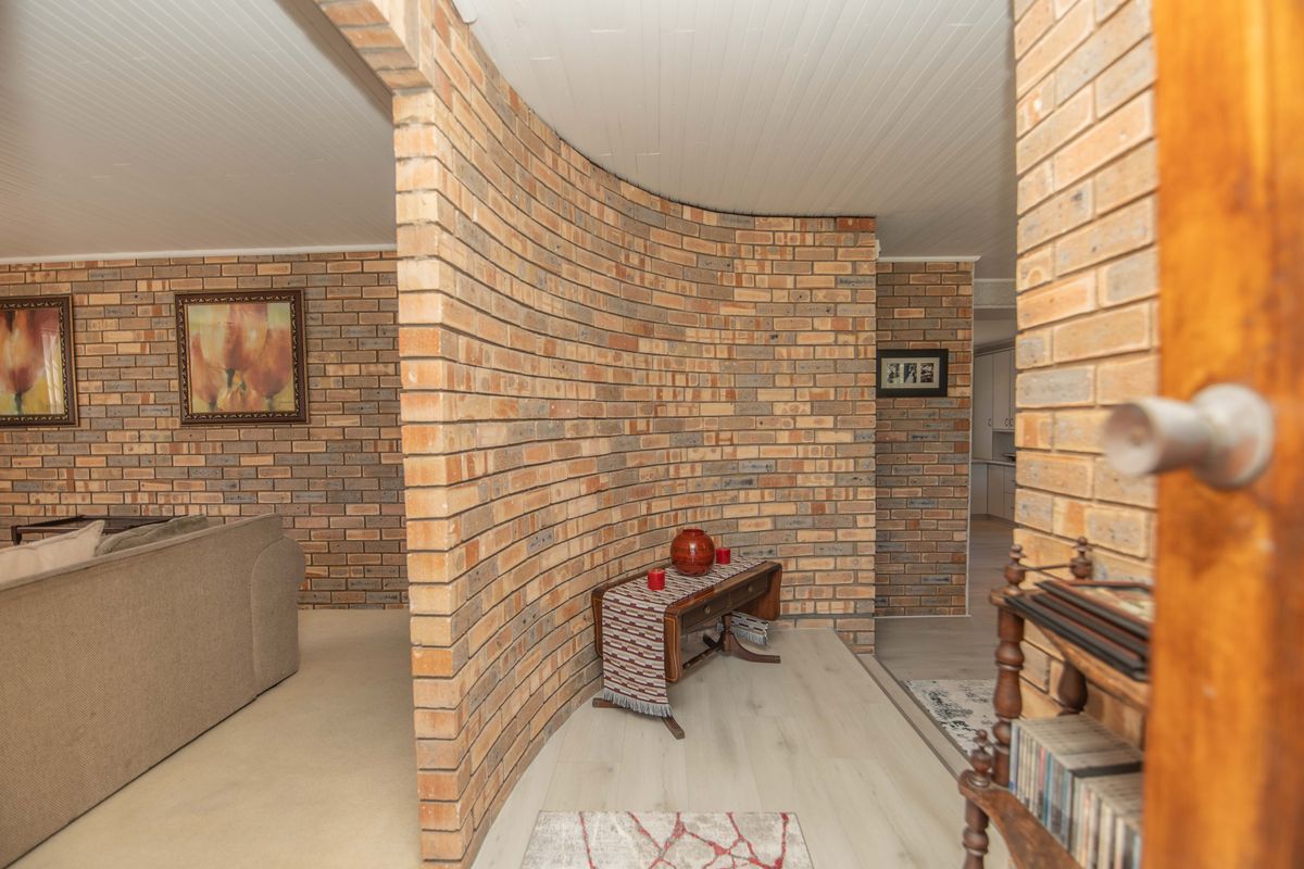 A living area featuring a distinctive curved face brick wall, light-toned laminate flooring, and a classic tongue and groove ceiling.