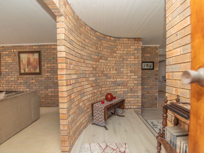 A living area featuring a distinctive curved face brick wall, light-toned laminate flooring, and a classic tongue and groove ceiling.