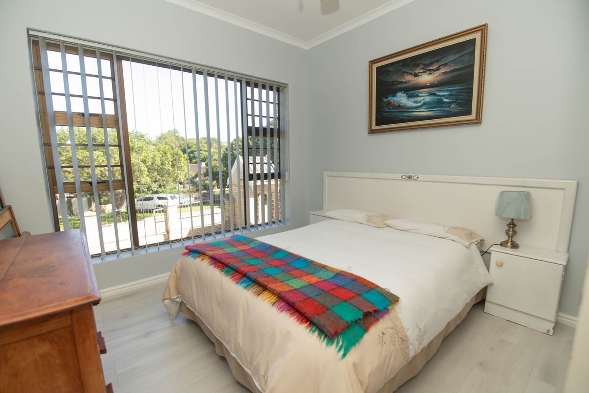 A well-maintained bedroom featuring light-toned laminate flooring, a built-in headboard, and large windows fitted with vertical blinds.