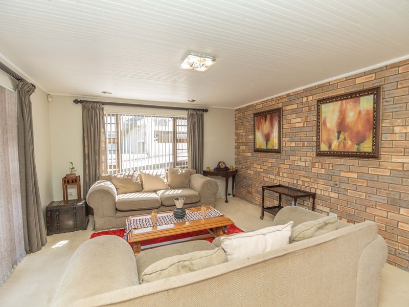 A comfortable living room featuring an exposed brick feature wall, tongue and groove ceiling, and large windows providing natural light.