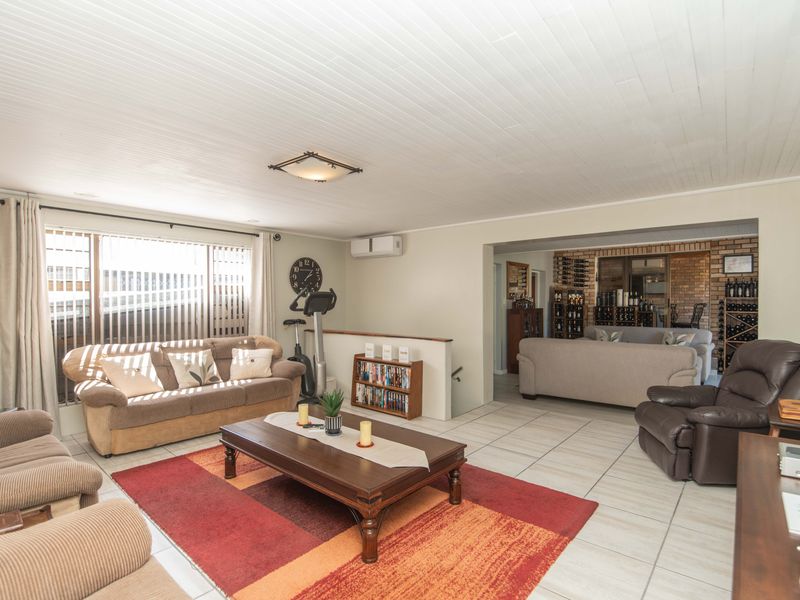 Spacious open-plan living area featuring tiled floors, a tongue and groove ceiling, split system air conditioning, and a brick feature wall with built-in wine storage.