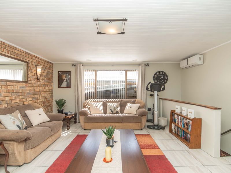 A living room featuring an exposed brick feature wall, tiled flooring, and a split-system air conditioner, with a staircase leading to a lower level.