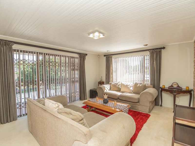Spacious living room featuring a brick accent wall, tongue and groove ceiling, and large sliding glass doors with security gates leading to the exterior.