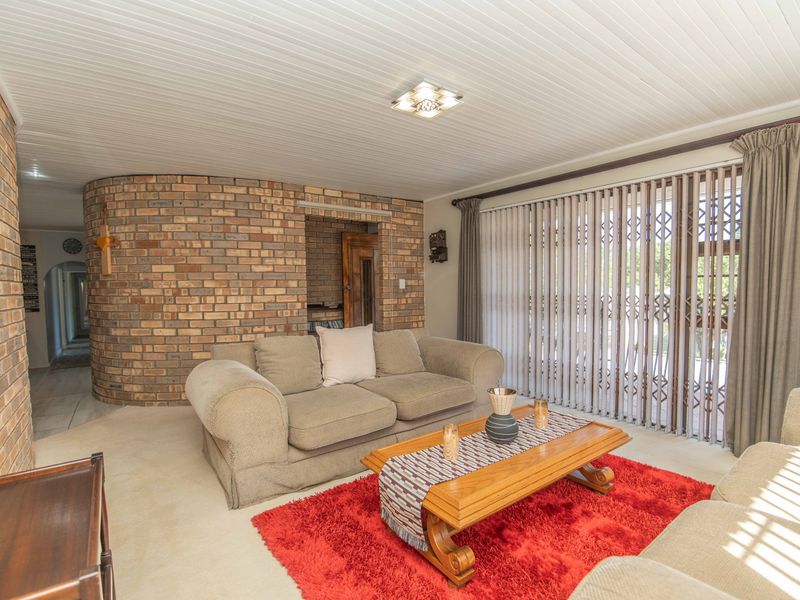 A living room featuring a distinctive curved exposed brick wall, tongue and groove ceiling, and large sliding doors with vertical blinds leading to the exterior.