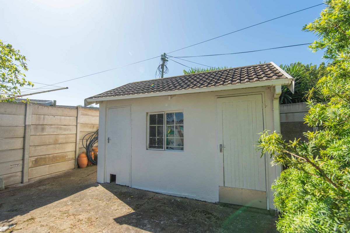 A detached outbuilding or storage structure featuring a tiled roof, timber doors, and a window, situated in a paved rear yard area.