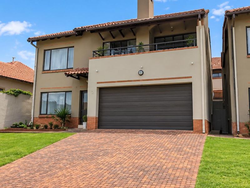 Front elevation of a double-story townhouse featuring a paved driveway, integrated double garage, and an upper-level balcony with a tiled roof.