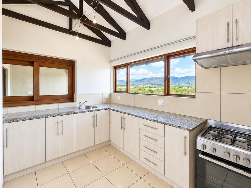 A bright, modern kitchen featuring granite countertops, gas stove, extractor fan, and exposed timber beams, offering scenic mountain views through large windows.