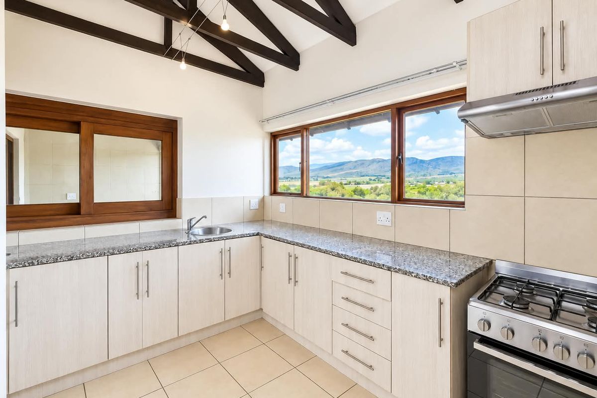 A bright, modern kitchen featuring granite countertops, gas stove, extractor fan, and exposed timber beams, offering scenic mountain views through large windows.