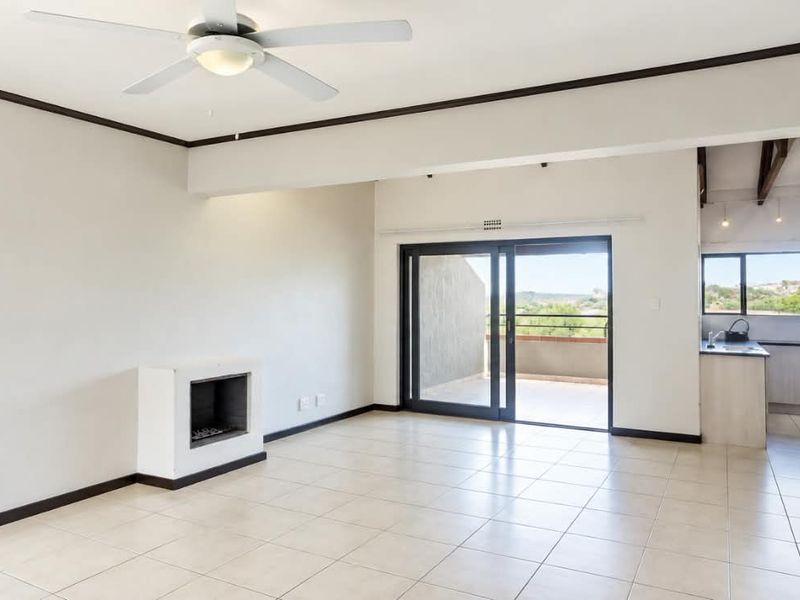 Spacious open-plan living area featuring tiled floors, a built-in fireplace, ceiling fan, and seamless access to an outdoor balcony.