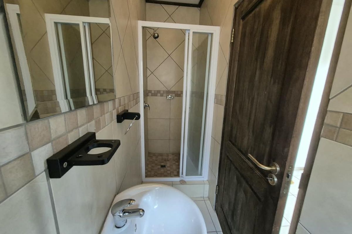 A compact bathroom featuring a shower enclosure, wall-mounted basin, and neutral tiled finishes throughout.