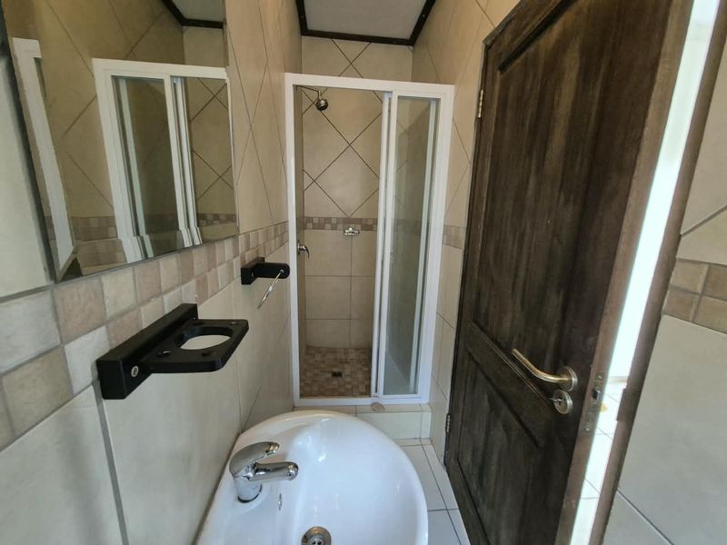 A compact bathroom featuring a shower enclosure, wall-mounted basin, and neutral tiled finishes throughout.