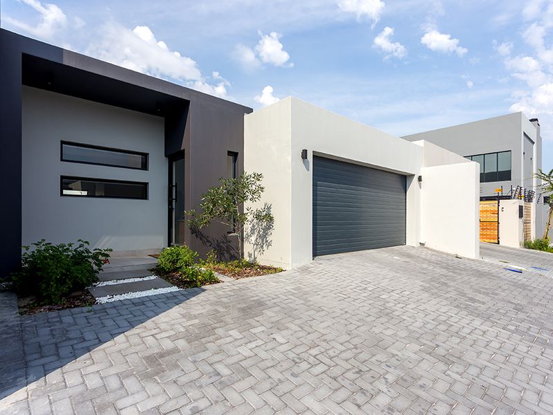 Modern front elevation featuring a paved driveway, a sleek sectional garage door, and a contemporary recessed entrance with clean architectural lines.