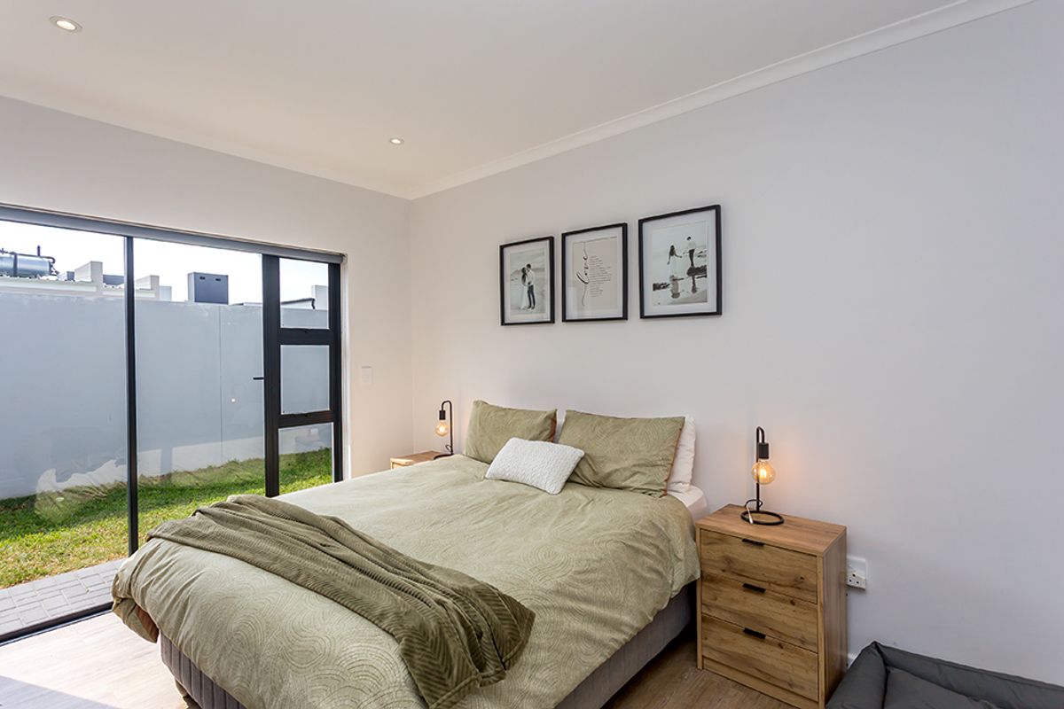 A bright and modern bedroom featuring laminate flooring, recessed downlights, and a large sliding glass door providing direct access to the garden.